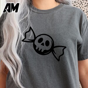 May include: Dark gray t-shirt featuring a black candy graphic with a skull design. The graphic is centered on the shirt. The shirt has short sleeves and a crew neck. The letters "AM" are in the upper left corner.