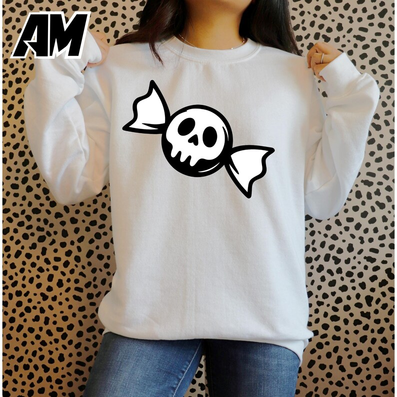 May include: White sweatshirt featuring a black and white candy design with a skull face. The long-sleeved top is a casual style, perfect for Halloween or spooky-themed events. The sweatshirt is a comfortable, everyday wear item.