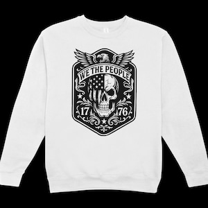 Puede incluir: Sudadera blanca con un gr&aacute;fico en blanco y negro. El gr&aacute;fico incluye una calavera con un dise&ntilde;o de la bandera estadounidense, el texto "WE THE PEOPLE", los n&uacute;meros "17" y "76", y un &aacute;guila.