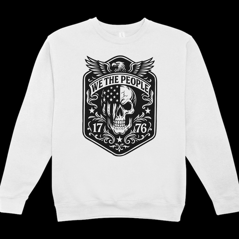 Puede incluir: Sudadera blanca con un gr&aacute;fico en blanco y negro. El gr&aacute;fico incluye una calavera con un dise&ntilde;o de la bandera estadounidense, el texto "WE THE PEOPLE", los n&uacute;meros "17" y "76", y un &aacute;guila.