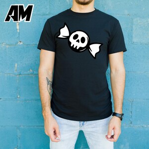 May include: Black t-shirt featuring a white skull candy graphic. The design shows a skull with a candy wrapper. The shirt is a crew neck style. The letters "AM" are in the upper left corner.