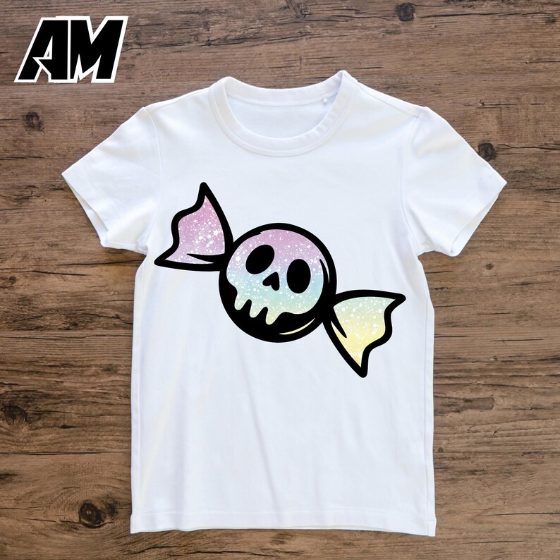 May include: White t-shirt featuring a candy-shaped skull design. The skull has a rainbow gradient, and the candy wrapper is black with pink and yellow accents. The shirt has short sleeves and a crew neck.