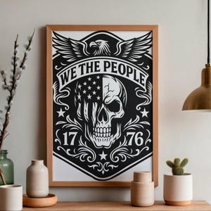 Puede incluir: Un estampado en blanco y negro enmarcado con un dise&ntilde;o de calavera con un motivo de bandera estadounidense. La impresi&oacute;n incluye el texto "WE THE PEOPLE" y los n&uacute;meros "1776". Un &aacute;guila con las alas extendidas est&aacute; en la parte superior del dise&ntilde;o. El marco es de madera.