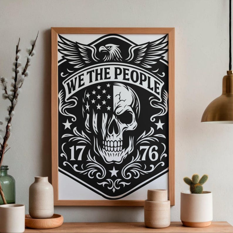 Puede incluir: Un estampado en blanco y negro enmarcado con un dise&ntilde;o de calavera con un motivo de bandera estadounidense. La impresi&oacute;n incluye el texto "WE THE PEOPLE" y los n&uacute;meros "1776". Un &aacute;guila con las alas extendidas est&aacute; en la parte superior del dise&ntilde;o. El marco es de madera.