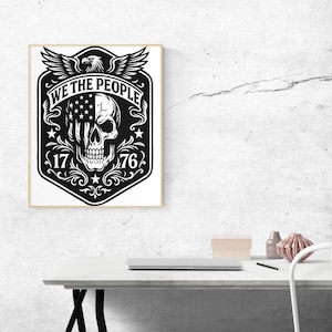 Puede incluir: Impresi&oacute;n art&iacute;stica enmarcada en blanco y negro con una calavera con el dise&ntilde;o de la bandera estadounidense en un lado. Las palabras "WE THE PEOPLE" est&aacute;n sobre la calavera, con los n&uacute;meros "1776" debajo. Un &aacute;guila con las alas extendidas est&aacute; en la parte superior.
