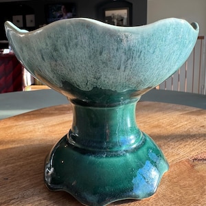 May include: A large, green and white ceramic bowl with a scalloped rim and a pedestal base. The bowl has a mottled glaze with a white and green color scheme.