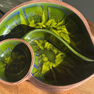 May include: A green and yellow ceramic serving dish with a divided section. The dish has a unique swirl pattern and is perfect for serving snacks or dips.