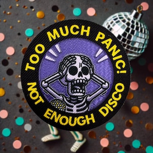 May include: A black and yellow embroidered patch with a skeleton holding its head in its hands and a disco ball. The text on the patch reads "Too Much Panic! Not Enough Disco."