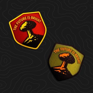 May include: Two shield-shaped embroidered patches featuring a mushroom cloud graphic and the text THE FUTURE IS BRIGHT. One patch has a red background with yellow text and border, while the other has an olive green background with orange text.