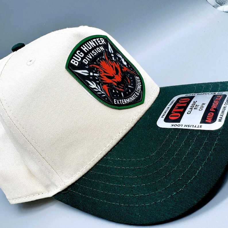 May include: A white and dark green baseball cap with a patch that reads "Bug Hunter Division" and a red and black graphic. The cap has a curved brim and a "Stylish Look" sticker.