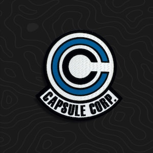 May include: A circular embroidered patch featuring a white and blue Capsule Corp. logo. The design includes a large black letter C inside a white circle with a blue ring, and the text CAPSULE CORP. in black capital letters on a white banner.