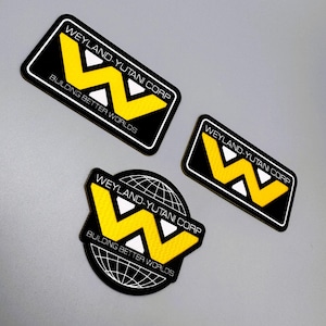 May include: Three embroidered patches featuring the Weyland-Yutani Corp logo. The patches are black with yellow and white accents. Text on the patches reads "WEYLAND-YUTANI CORP" and "BUILDING BETTER WORLDS". One patch is circular with a globe.