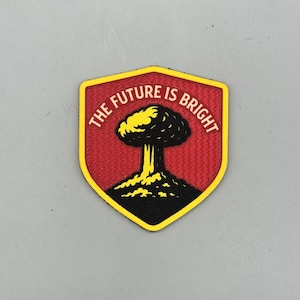 May include: A shield-shaped patch with the text "THE FUTURE IS BRIGHT" in white. The patch features a yellow and black atomic explosion design on a red background, with a yellow border.