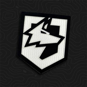 May include: A shield-shaped embroidered patch featuring a stylized wolf head graphic in high-contrast black and white thread. The design consists of sharp, geometric lines forming the wolf silhouette against a solid black background.