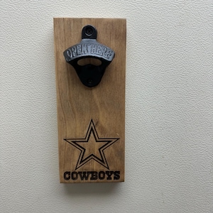 Peut inclure: Un ouvre-bouteille en bois avec un ouvre-bouteille en métal noir et le logo des Dallas Cowboys ainsi que les mots "COWBOYS" gravés sur le bois.