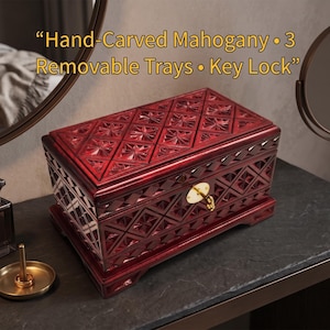 May include: A hand-carved mahogany jewellery box with three removable trays and a key lock. The box is a deep red colour with intricate geometric carvings. The text on the image reads: "Hand-Carved Mahogany • 3 Removable Trays • Key Lock."