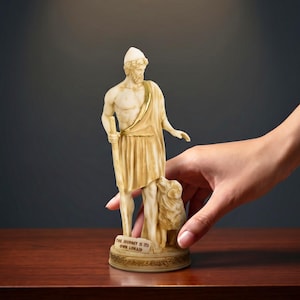May include: An alabaster statuette of a bearded figure wearing a cap and draped garment, holding a staff with a small animal at their side. The base features the text "THE JOURNEY IS ITS OWN LONAID" and the image includes the text "epic history. timeless art."