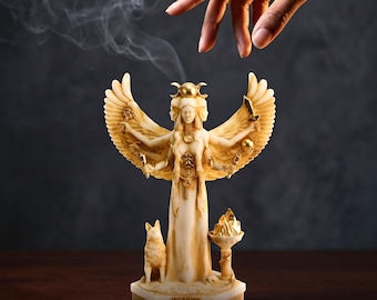 May include: An off-white alabaster statue of a three-faced deity with large wings, holding various items in multiple arms. The figure features gold-colored accents, a dog at its side, and a small pedestal with a flame. Text reads: for when magic calls.