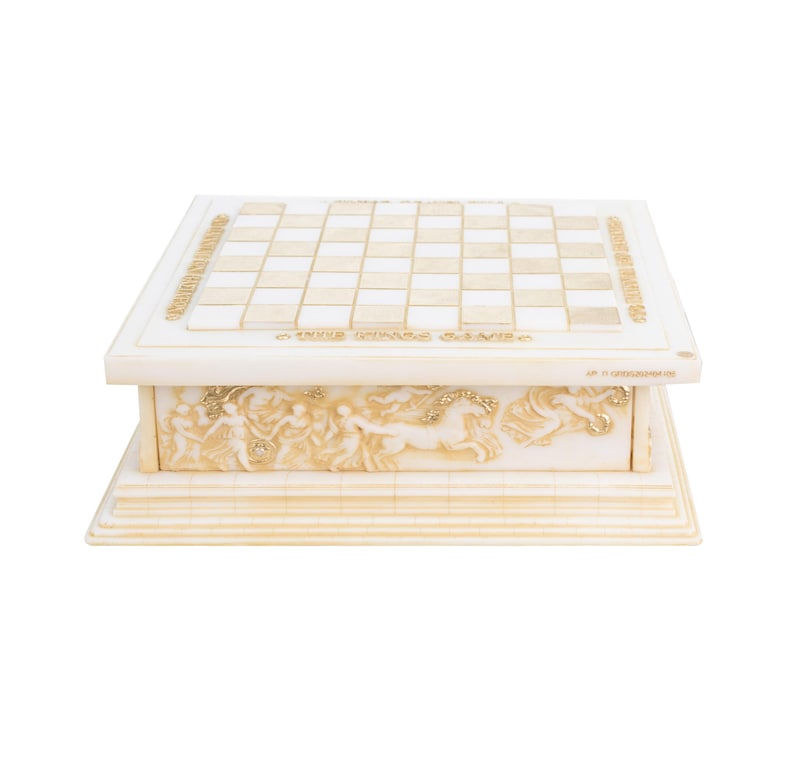 K&ouml;nnte beinhalten: Ein cremefarbenes Schachspiel mit einem Schachbrettmuster und einem dekorativen Sockel. Der Sockel zeigt Reliefs von Figuren und Pferden. Die Worte "THE CHESS GAME" sind auf der Vorderseite des Sets zu sehen.
