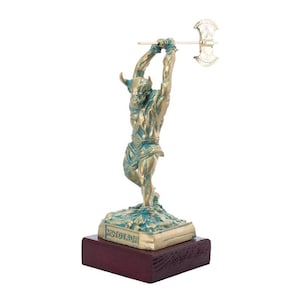 May include: A bronze statue of a minotaur holding an axe, standing on a green base with the word "Minotaur" inscribed on it. The statue is on a wooden base.