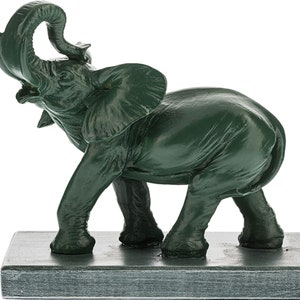 May include: A green ceramic elephant figurine with its trunk raised in the air. The elephant is standing on a square base.