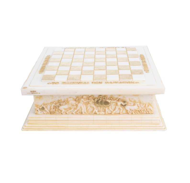 K&ouml;nnte beinhalten: Ein dekoratives Schachspiel in Creme- und Goldt&ouml;nen. Das Schachbrett hat ein Rastermuster, und die Basis ist mit Reliefskulpturen von Figuren und Text verziert. Das Set besteht aus einem hellen Material.