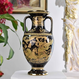 Puede incluir: Jarrón de cerámica negro y dorado con un diseño de clave griega y una escena de una criatura mítica con un caballo y una figura humana. El jarrón tiene dos asas.