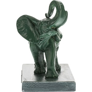 May include: Green ceramic elephant figurine with its trunk raised in the air. The elephant is standing on a square base.