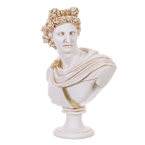 Puede incluir: Busto de yeso blanco de un hombre con el pelo rizado y un ribete dorado en la tela. El busto está sobre un pedestal blanco.