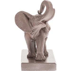 May include: A brown ceramic elephant figurine with its trunk raised in the air. The elephant is standing on a rectangular base.