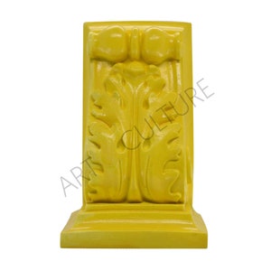 May include: A yellow wooden corbel with a carved floral design. The corbel has a square base and a rectangular top.