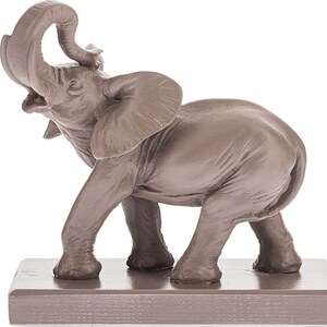 May include: A brown ceramic elephant figurine with its trunk raised in the air. The elephant is standing on a small, rectangular base.
