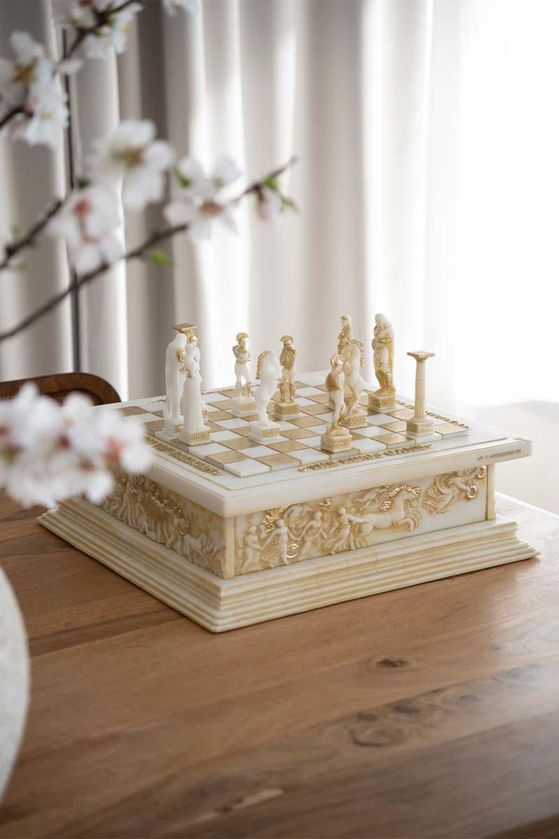 K&ouml;nnte beinhalten: Ein dekoratives Schachspiel mit Elfenbein- und Goldakzenten. Das Schachbrett ist quadratisch mit einem Schachbrettmuster. Die Schachfiguren sind geformte Figuren. Der Sockel des Schachspiels zeigt Reliefschnitzereien klassischer Figuren und Pferde.