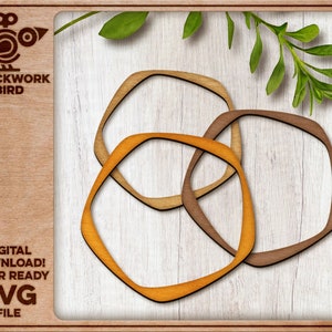 May include: Three interlocking wooden shapes in orange, brown, and light brown, resembling a geometric design. The shapes are cut out and layered on a white wood background.