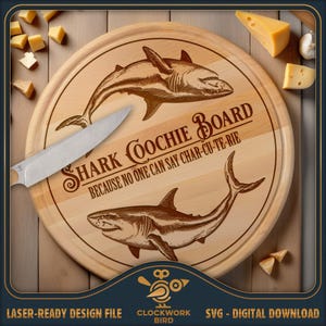 Peut inclure: Une planche de service ronde en bois avec des illustrations gravées au laser de deux requins et le texte SHARK COOCHIE BOARD BECAUSE NO ONE CAN SAY CHAR-CU-TE-RIE. Un couteau en métal argenté repose en diagonale sur la surface en bois.