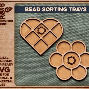 May include: Two wooden bead sorting trays, one shaped like a heart and the other like a flower. Both trays have a decorative design in the centre and are laser cut.