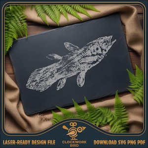 Puede incluir: Una tabla rectangular de pizarra gris oscuro con una ilustración grabada detallada de un pez celacanto. El diseño blanco del pez está en ángulo sobre la tabla. Helechos verdes y un paño marrón rodean la tabla.