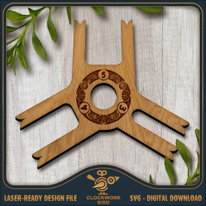 May include: A wooden laser-cut game piece with a circular centre and three arms. The centre has a decorative design and the numbers 3, 4, and 5 around the circle. The piece is on a woodgrain background.
