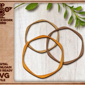 May include: Three interlocking wooden rings in shades of brown and orange. The rings are cut out in a simple, geometric shape. The rings are on a white wood background.