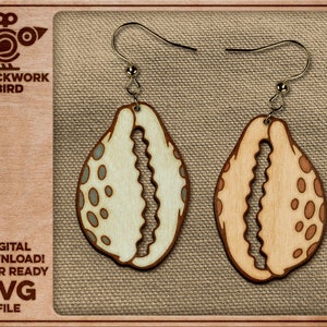 Puede incluir: Pendientes de madera con forma de concha, con un acabado de veta de madera clara y bordes marrones oscuros. Los pendientes tienen un diseño recortado y están adornados con pequeños puntos azul claro y marrón. El texto "CLOCKWORK BIRD" y "DIGITAL DOWNLOAD! LASER READY SVG FILE" son visibles.