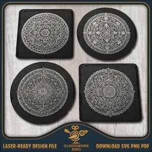 Puede incluir: Un juego de cuatro posavasos de pizarra negra con intrincados diseños de mandalas en blanco. Dos posavasos son cuadrados y dos son circulares. Cada pieza muestra un patrón floral simétrico detallado grabado en la superficie de piedra.
