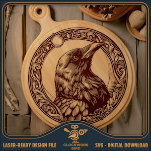 Könnte beinhalten: Ein rundes, hölzernes Schneidebrett mit einem lasergravierten Design eines Rabens in einem kreisförmigen Rahmen mit floralen Details. Der Rabe blickt nach rechts und hat ein detailliertes Design. Der Text "CLOCKWORK BIRD" ist unter dem Bild sichtbar.