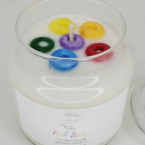 May include: A white candle with a label that reads "Fruit Loops" and "Stephanie's Scents". The candle is topped with colorful cereal rings.