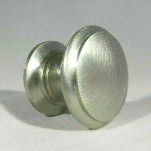 May include: A brushed nickel cabinet knob with a round, slightly raised design. The knob has a smooth, polished finish.