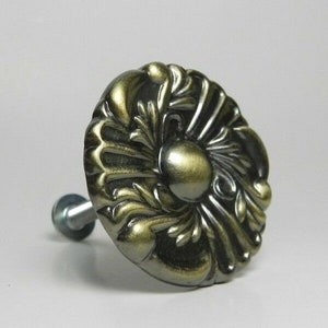 May include: A gold-toned metal knob with a decorative floral design. The knob has a screw on the back for attaching to a surface.