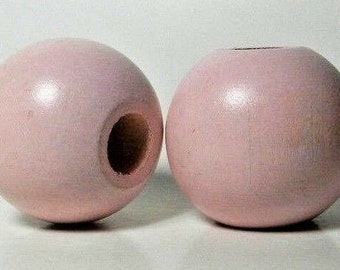 May include: Two large, round, wooden beads painted a light pink color. The beads have a hole through the center.