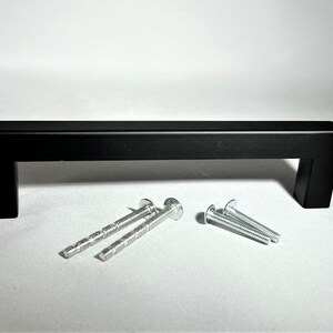 May include: Black metal cabinet door pull with square edges and rounded corners. The pull comes with two sets of screws for installation.