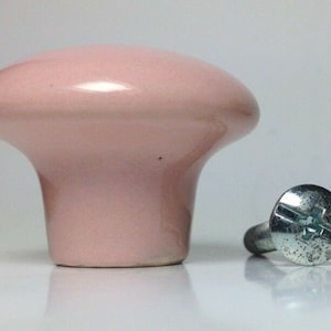 May include: A pale pink ceramic cabinet knob with a smooth, rounded surface and a matching screw.