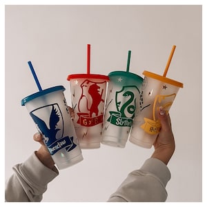 Puede incluir: Cuatro vasos de plástico transparente con diferentes escudos de las casas de Hogwarts. Los vasos están decorados con el león de Gryffindor, la serpiente de Slytherin, el tejón de Hufflepuff y el águila de Ravenclaw. Cada vaso tiene una tapa y una pajita de diferente color.