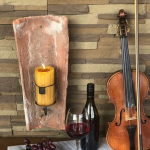 Può includere: Un vassoio da portata in marmo bianco con una selezione di formaggi, uva e un bicchiere di vino rosso. Una candela accesa si trova in un portacandele rustico in terracotta. Un violino e un arco sono sullo sfondo.